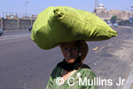 Caption: Modern Culture; Egyptian woman carrying large sack on her head down the street from the grand mosque